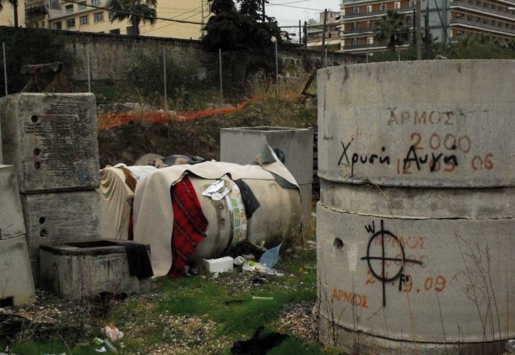 Inmigrantes durmiendo en tubos de hormigón en Atenas junto a una pintada del partido nazi Amanecer Dorado. Foto / Clara Palma.
